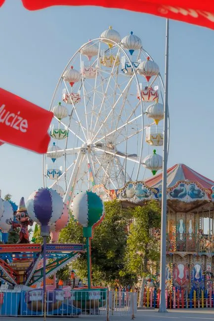 Colorful ferris wheel and rides at an amusement park under a clear blue sky.