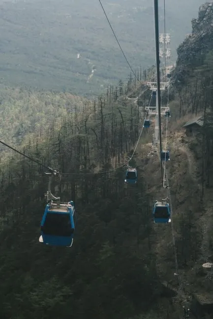 Aerial view of blue cable cars traveling up a forested mountain, capturing serene nature.