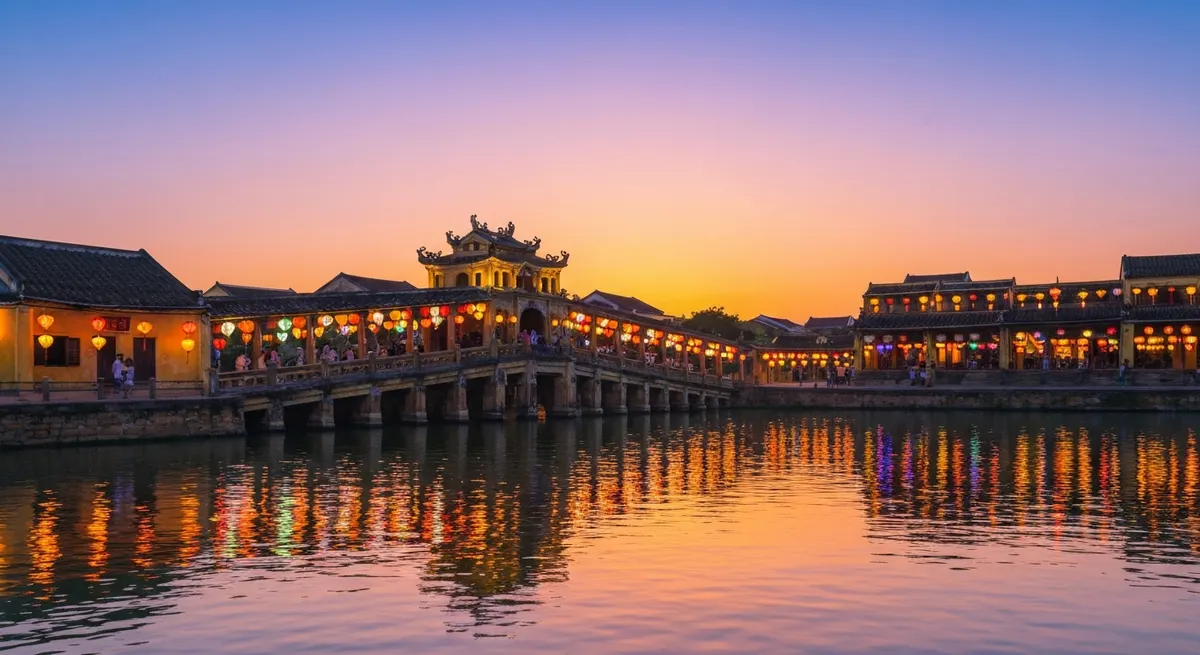 黄昏时分从怀河水边看会安日本廊桥,红黄灯笼的光芒在水面上闪烁,桥上行人身影绰绰